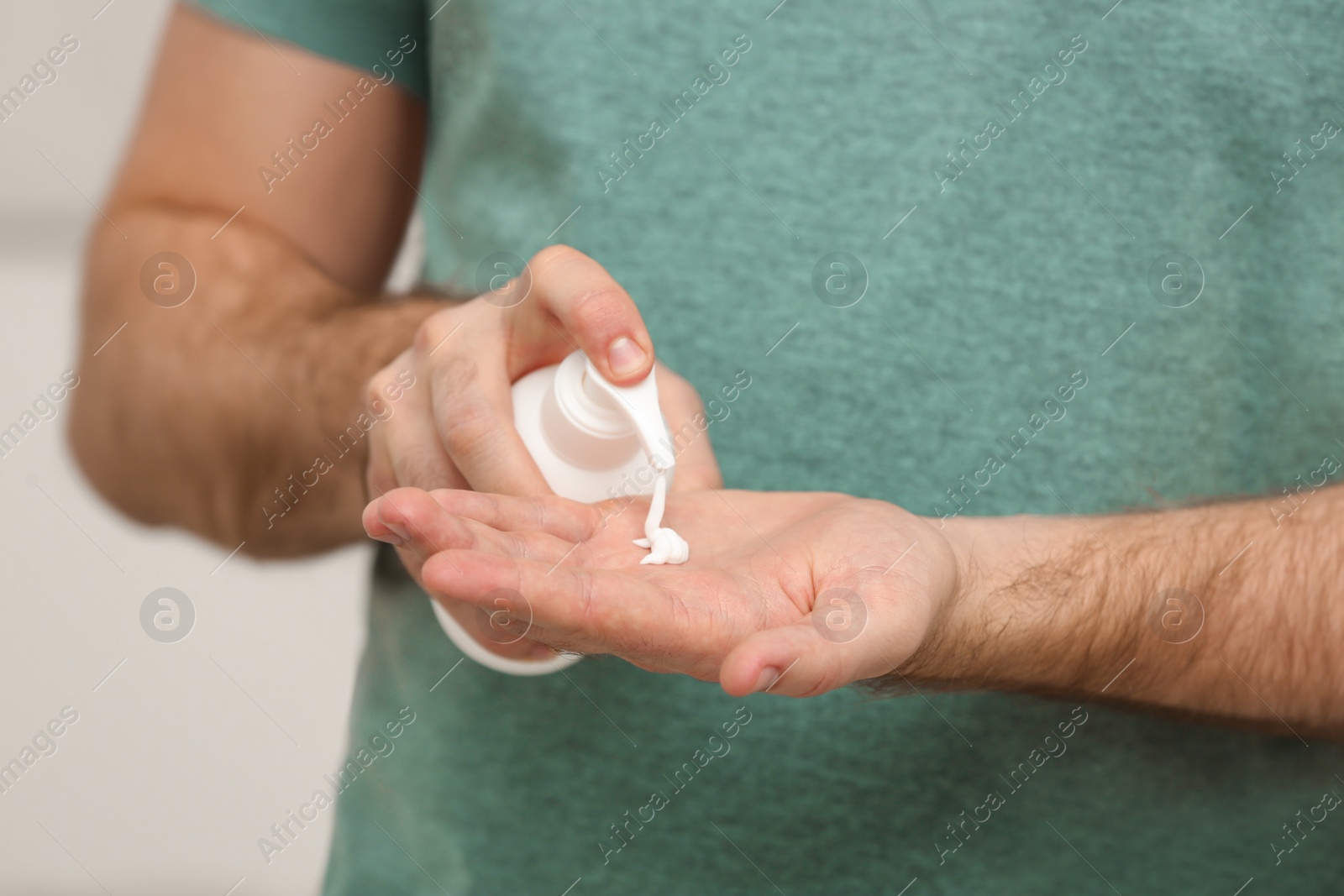 Photo of Man applying cream from dispenser onto hand on light grey background, closeup