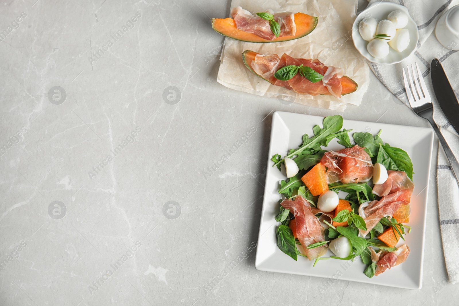 Photo of Flat lay composition of fresh melon with prosciutto on light grey marble table. Space for text