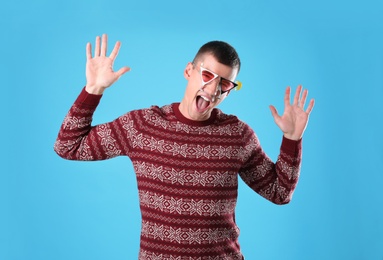 Photo of Emotional young man in Christmas sweater and party glasses on light blue background