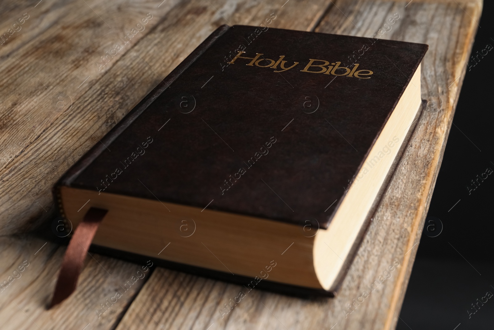 Photo of Bible with dark cover on wooden table. Christian religious book