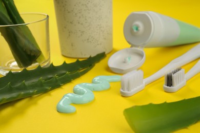 Photo of Aloe vera toothpaste, brushes and green leaves on yellow background