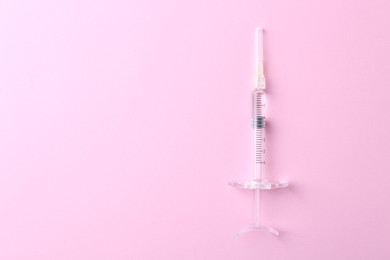 Cosmetology. Medical syringe on pink background, top view. Space for text