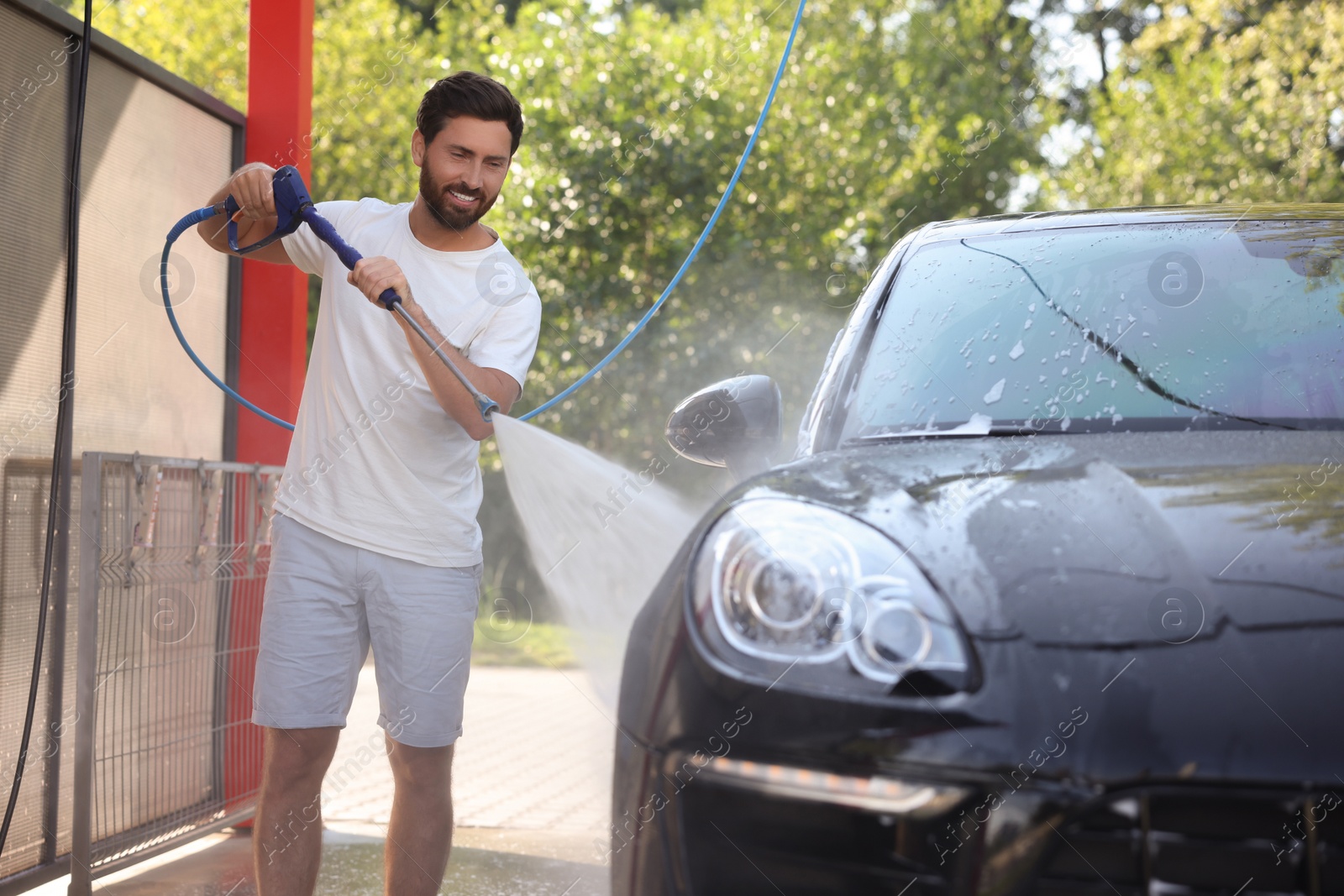 Photo of Happy man washing auto with high pressure water jet at outdoor car wash