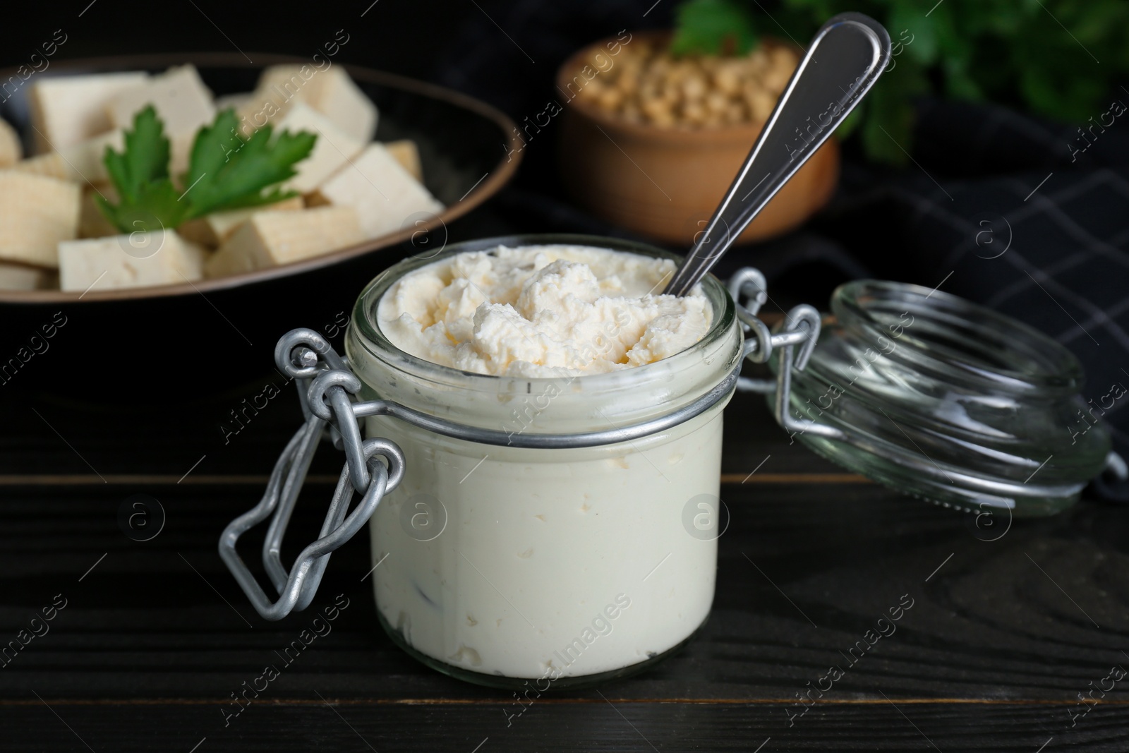 Photo of Delicious tofu cream cheese in glass jar on black wooden table, closeup