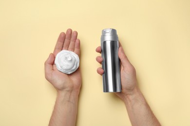 Man holding shaving foam and bottle on beige background, top view