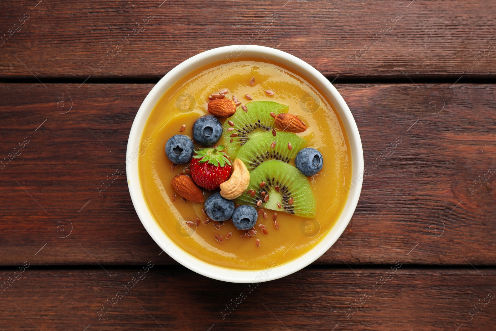 Photo of Delicious smoothie bowl with fresh berries, kiwi and nuts on wooden table, top view