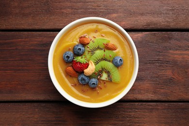 Photo of Delicious smoothie bowl with fresh berries, kiwi and nuts on wooden table, top view