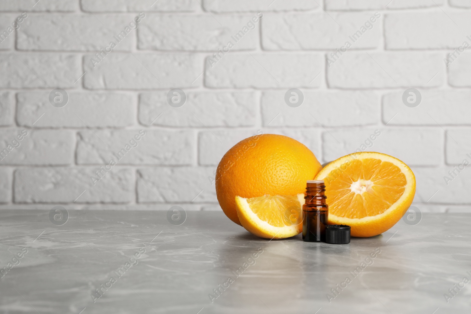 Photo of Bottle of essential oil with oranges on grey marble table against white brick wall. Space for text