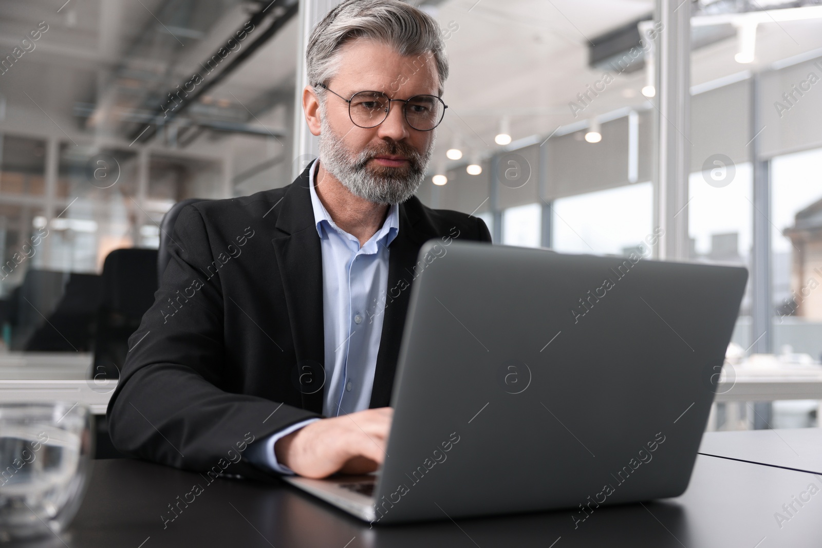 Photo of Handsome man working with laptop at table in office. Lawyer, businessman, accountant or manager