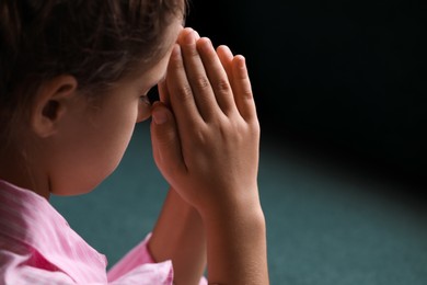 Photo of Cute little girl with hands clasped together praying on blurred background, closeup
