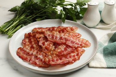 Photo of Plate with fried bacon slices and parsley on white table, closeup