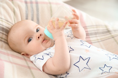 Pretty baby drinking from bottle on bed at home