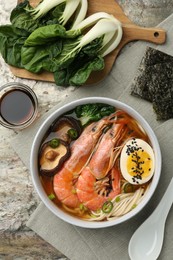 Photo of Delicious ramen with shrimps and egg in bowl served on grey textured table, flat lay. Noodle soup
