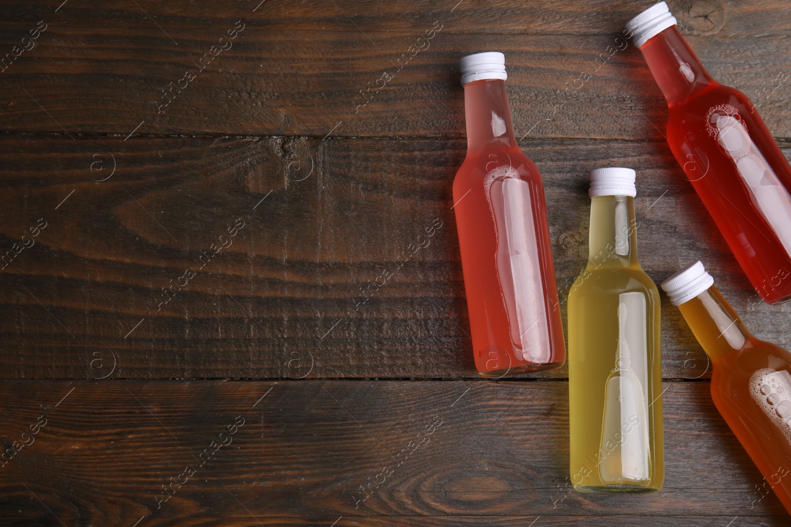 Photo of Delicious kombucha in glass bottles on wooden table, flat lay. Space for text