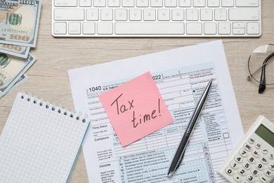 Reminder note with words Tax Time, documents, computer keyboard, money and calculator on white wooden table, flat lay