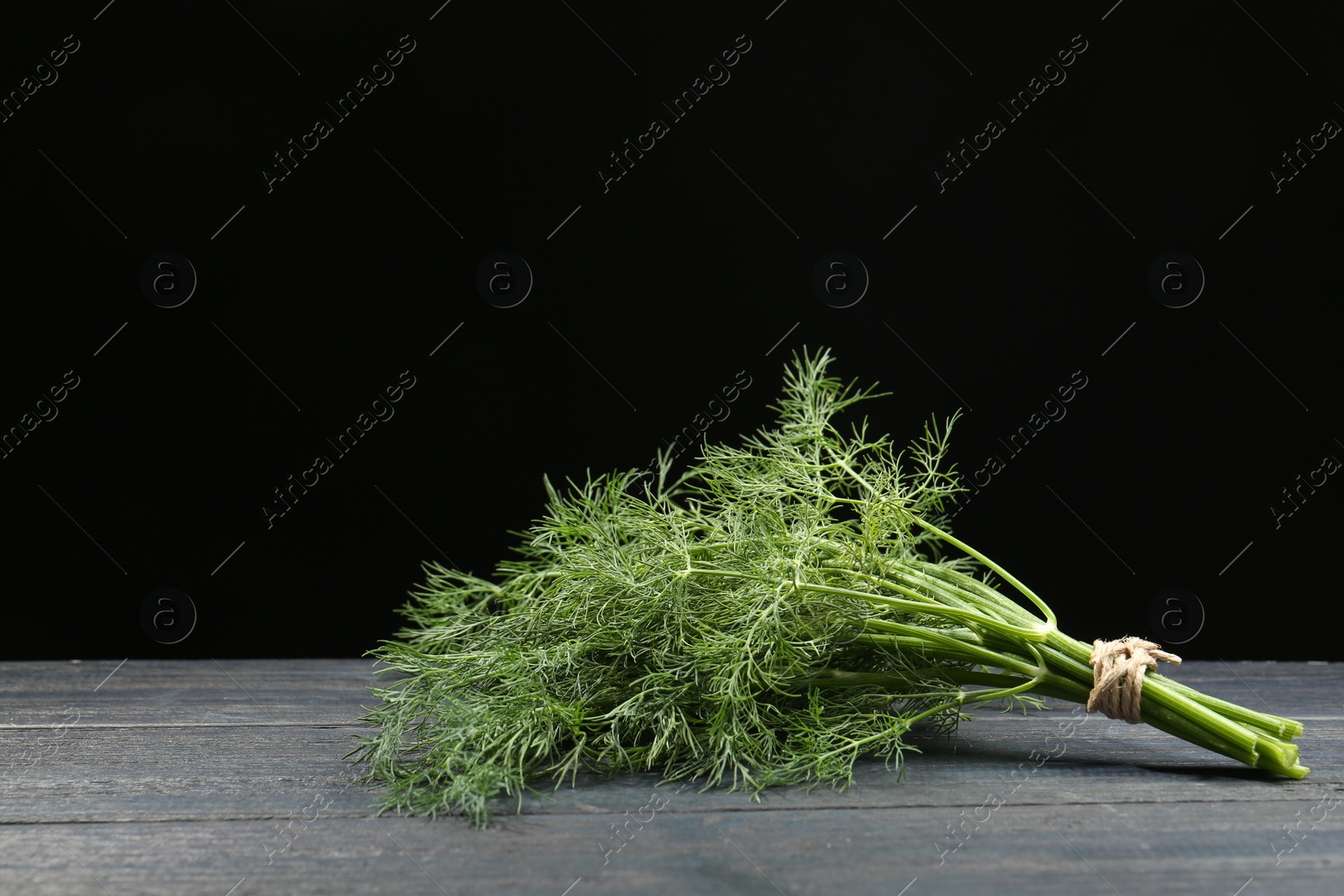 Photo of Bunch of fresh green dill on grey wooden table against black background