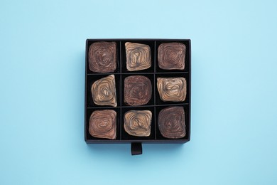 Photo of Box of tasty chocolate candies on light blue background, top view