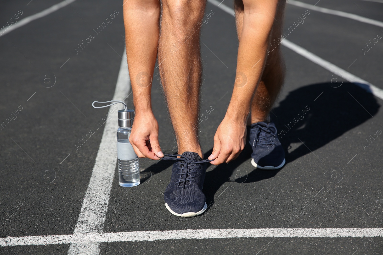 Photo of Sporty man tying shoelaces before running at stadium on sunny morning