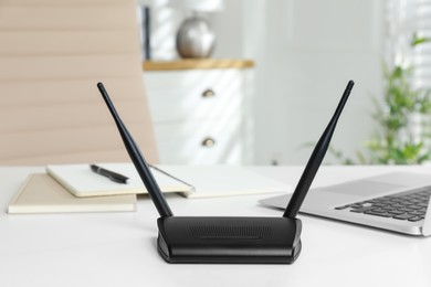 Photo of Modern wi-fi router and laptop on white table indoors