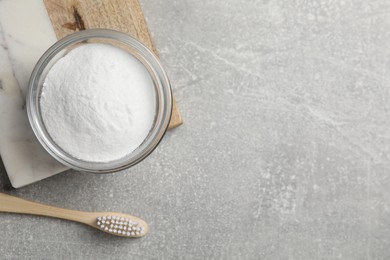 Bamboo toothbrush and bowl of baking soda on grey table, flat lay. Space for text