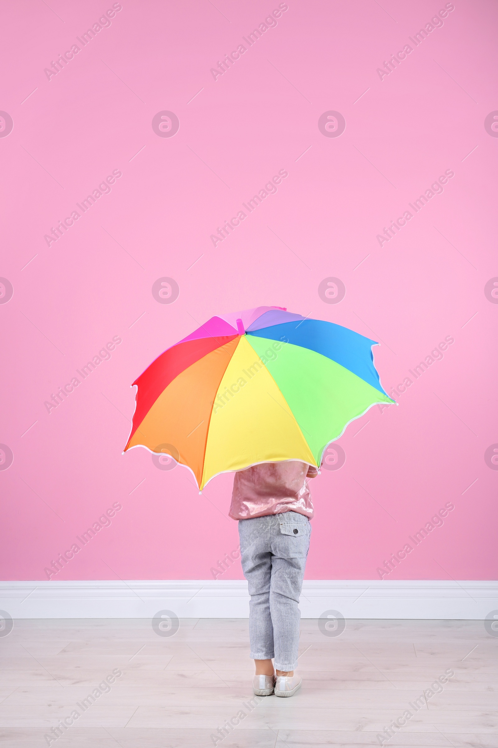 Photo of Little girl with rainbow umbrella near color wall. Space for text