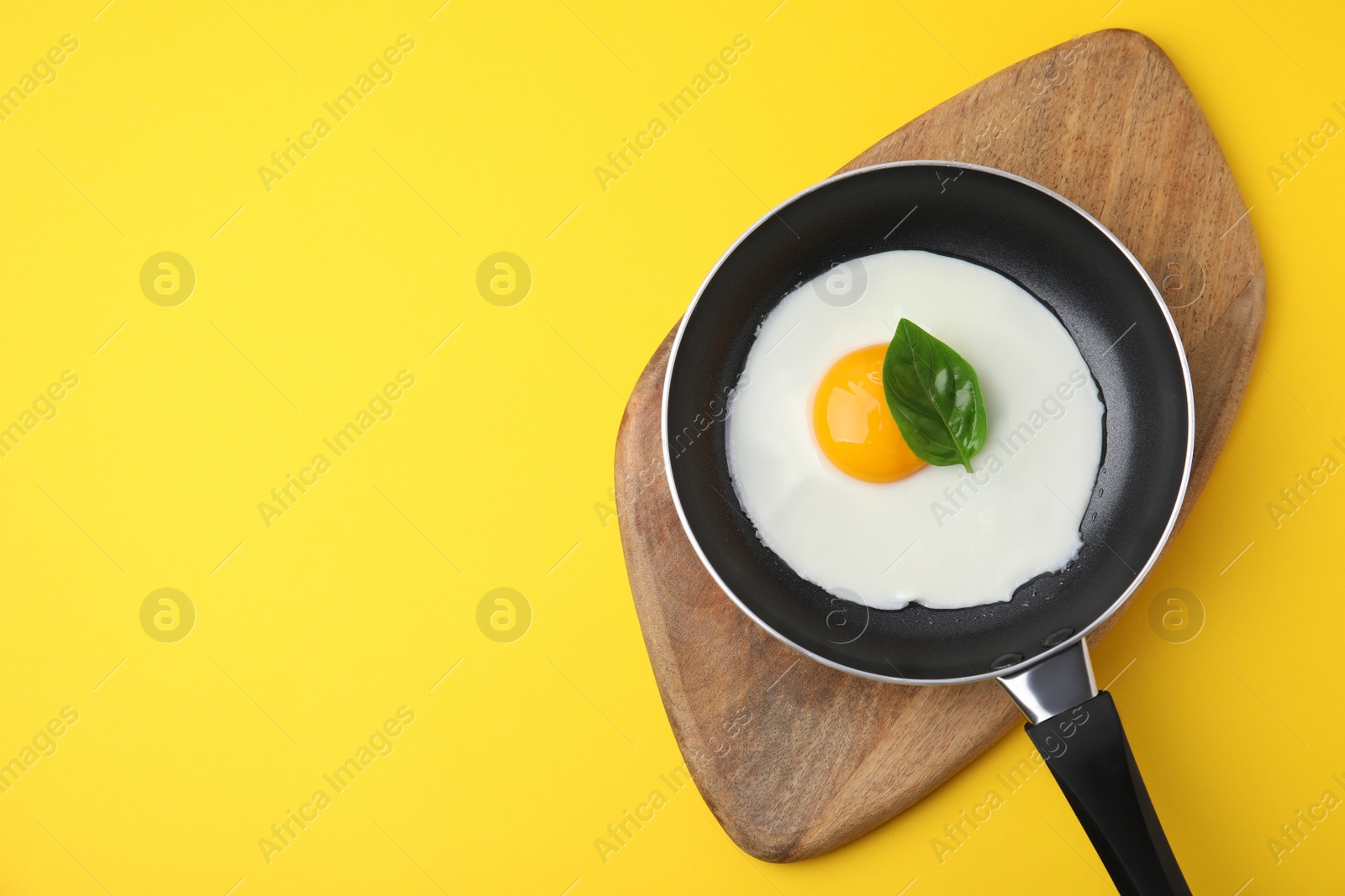Photo of Pan with tasty fried egg on yellow background, top view. Space for text