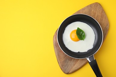 Pan with tasty fried egg on yellow background, top view. Space for text