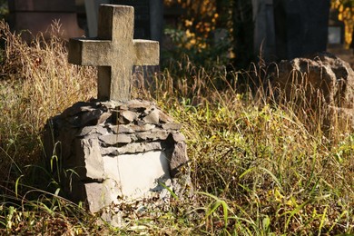 Photo of Old concrete tombstone with cross on cemetery, space for text. Funeral ceremony