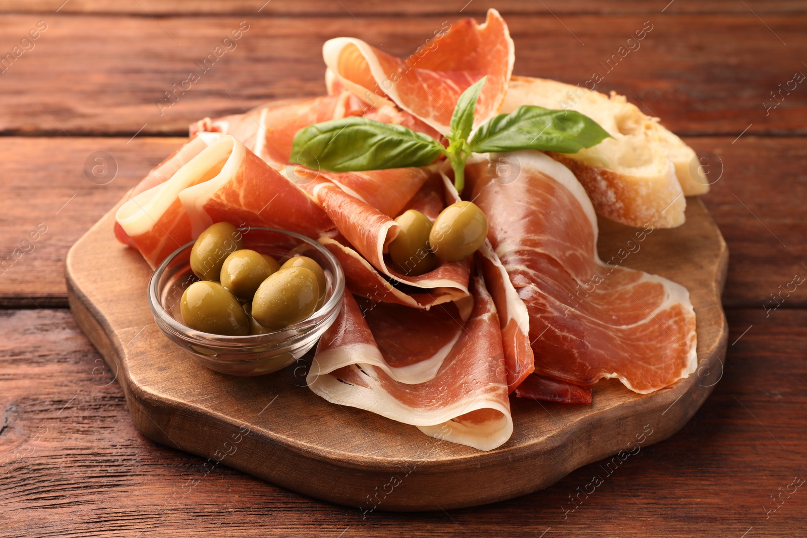 Photo of Slices of tasty cured ham, olives, bread and basil on wooden table, closeup