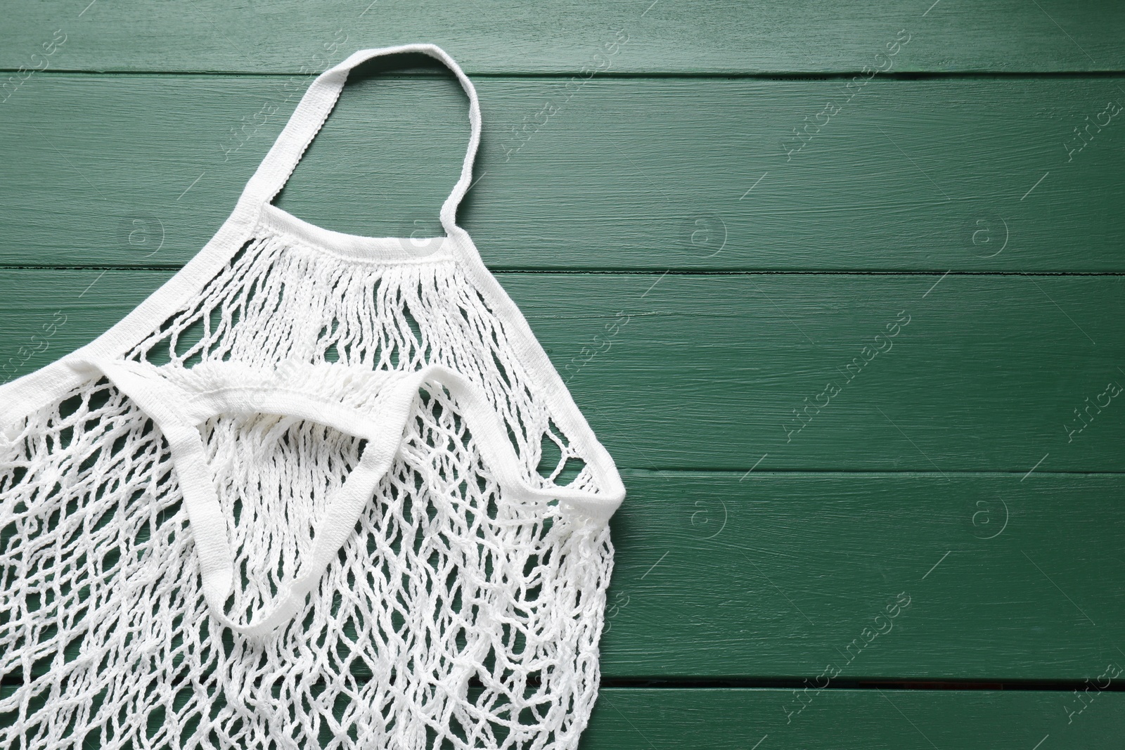 Photo of White string bag on green wooden table, top view. Space for text