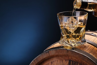 Pouring whiskey from bottle into glass on wooden barrel against blue background, closeup. Space for text