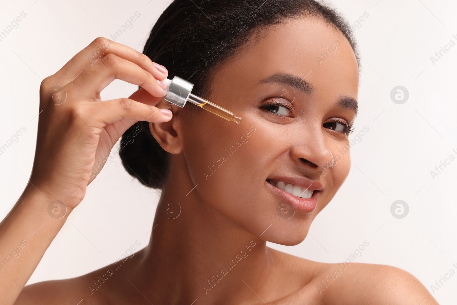Photo of Smiling woman applying serum onto her face on white background, closeup