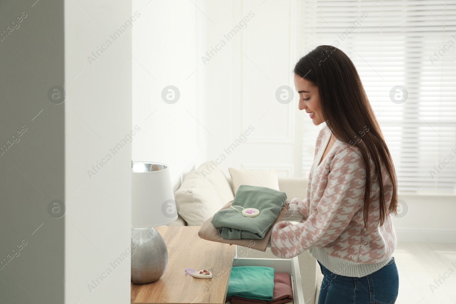 Photo of Woman with scented sachet and clothes near chest of drawers in room