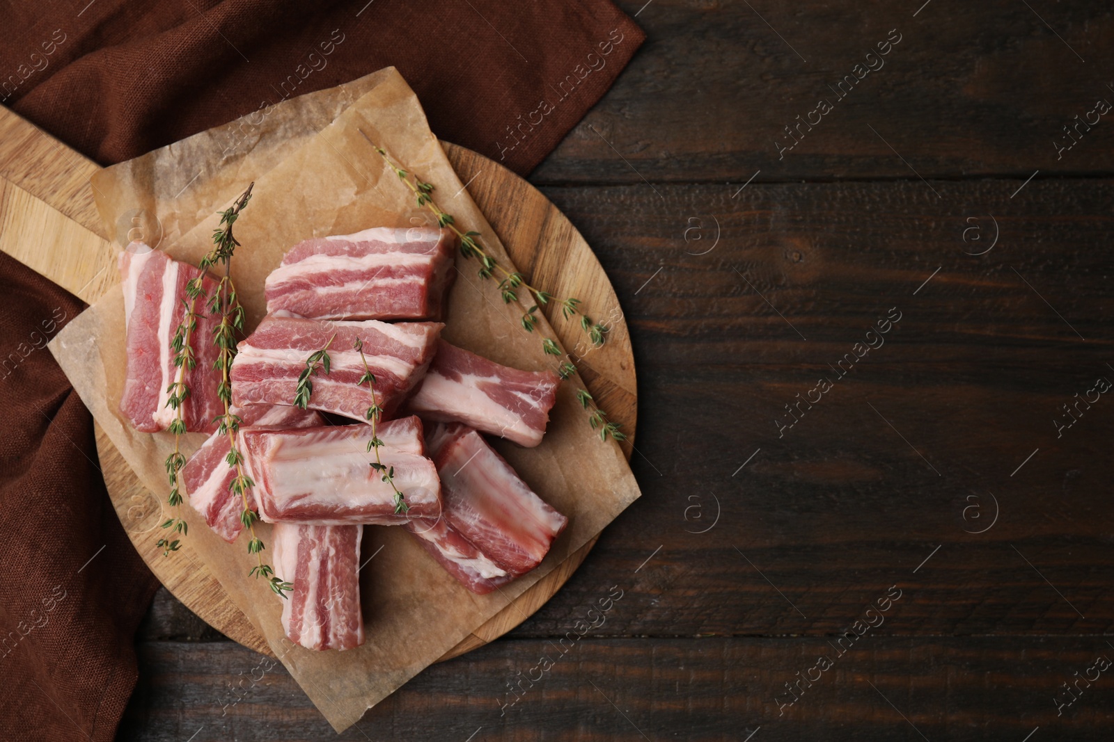 Photo of Cut raw pork ribs with thyme on wooden table, top view. Space for text