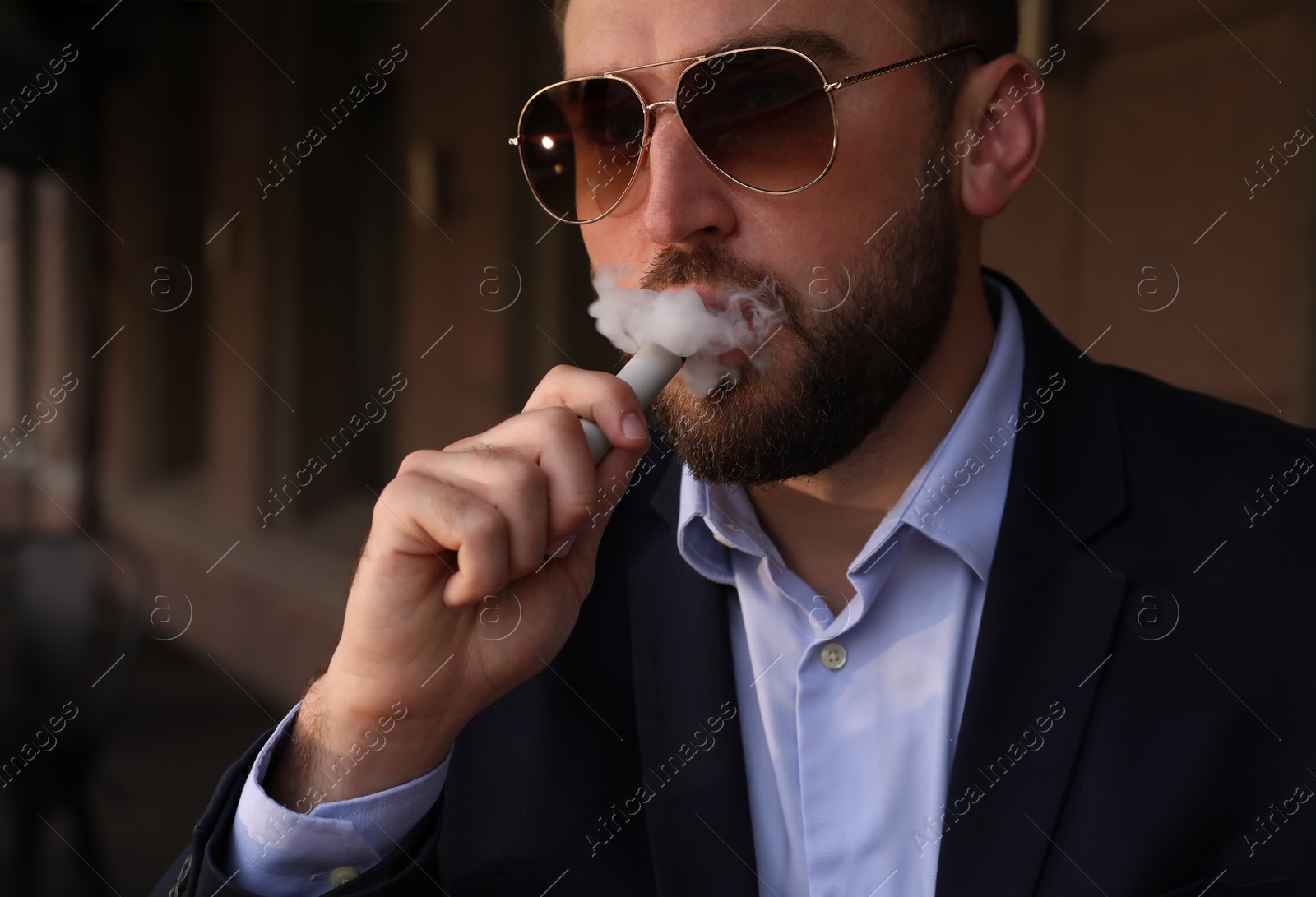 Photo of Handsome young businessman using disposable electronic cigarette outdoors