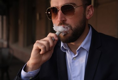 Handsome young businessman using disposable electronic cigarette outdoors