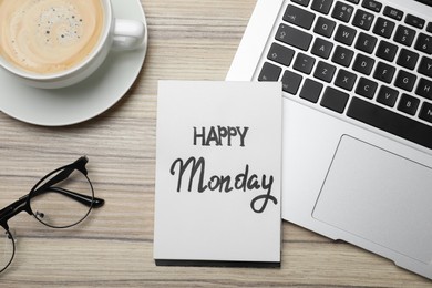 Message Happy Monday written in notebook, laptop and cup of coffee on wooden desk, flat lay