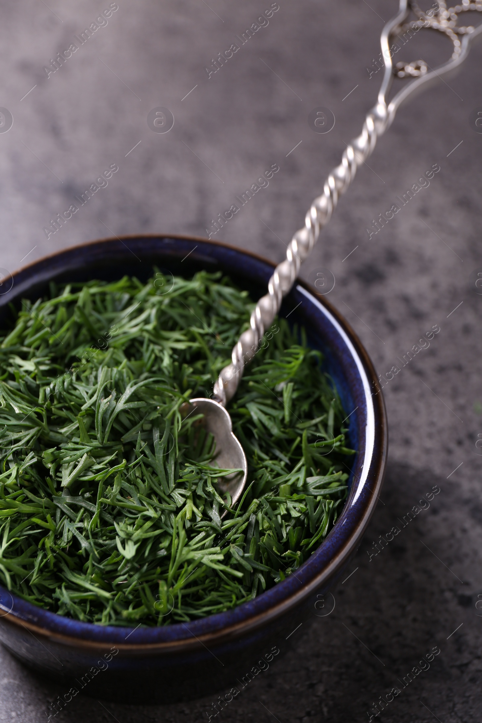 Photo of Fresh cut dill in bowl and spoon on grey textured table, closeup