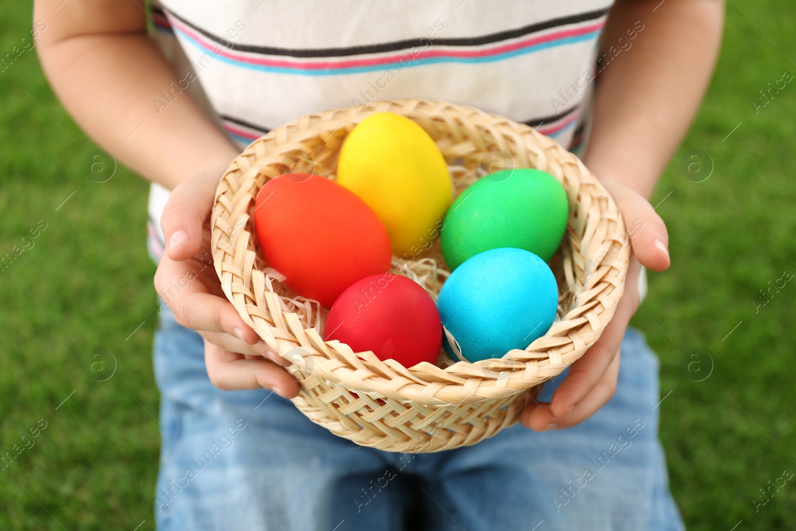 Photo of Cute little boy with basket full of Easter eggs outdoors, closeup