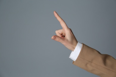 Photo of Businesswoman pointing at something on grey background, closeup. Finger gesture