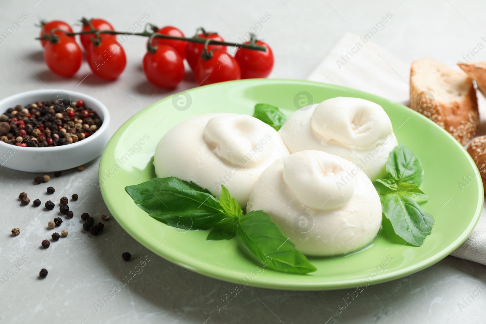 Photo of Delicious burrata cheese with basil and spices on light table, closeup