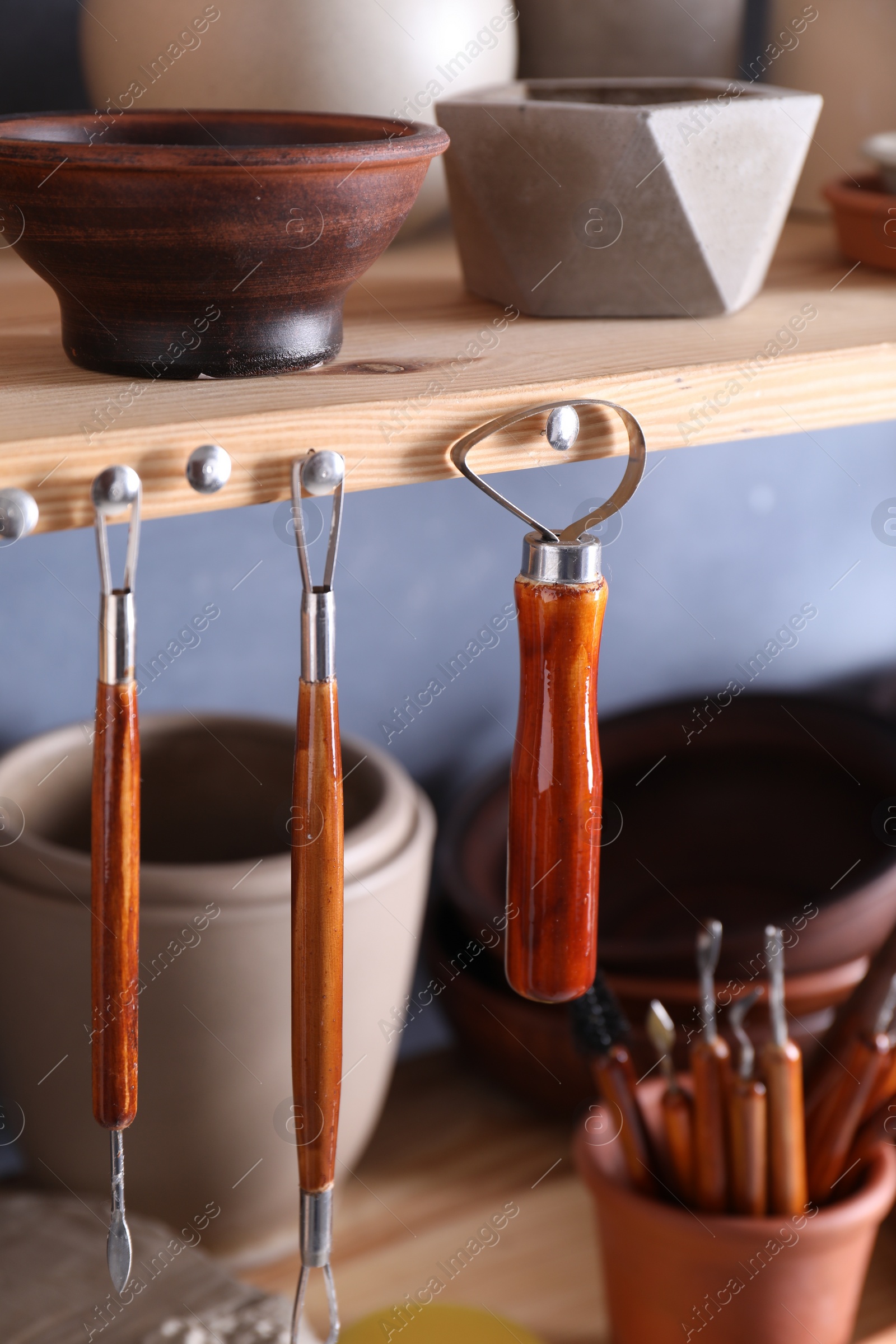 Photo of Set of different crafting tools and clay dishes on wooden rack in workshop, closeup