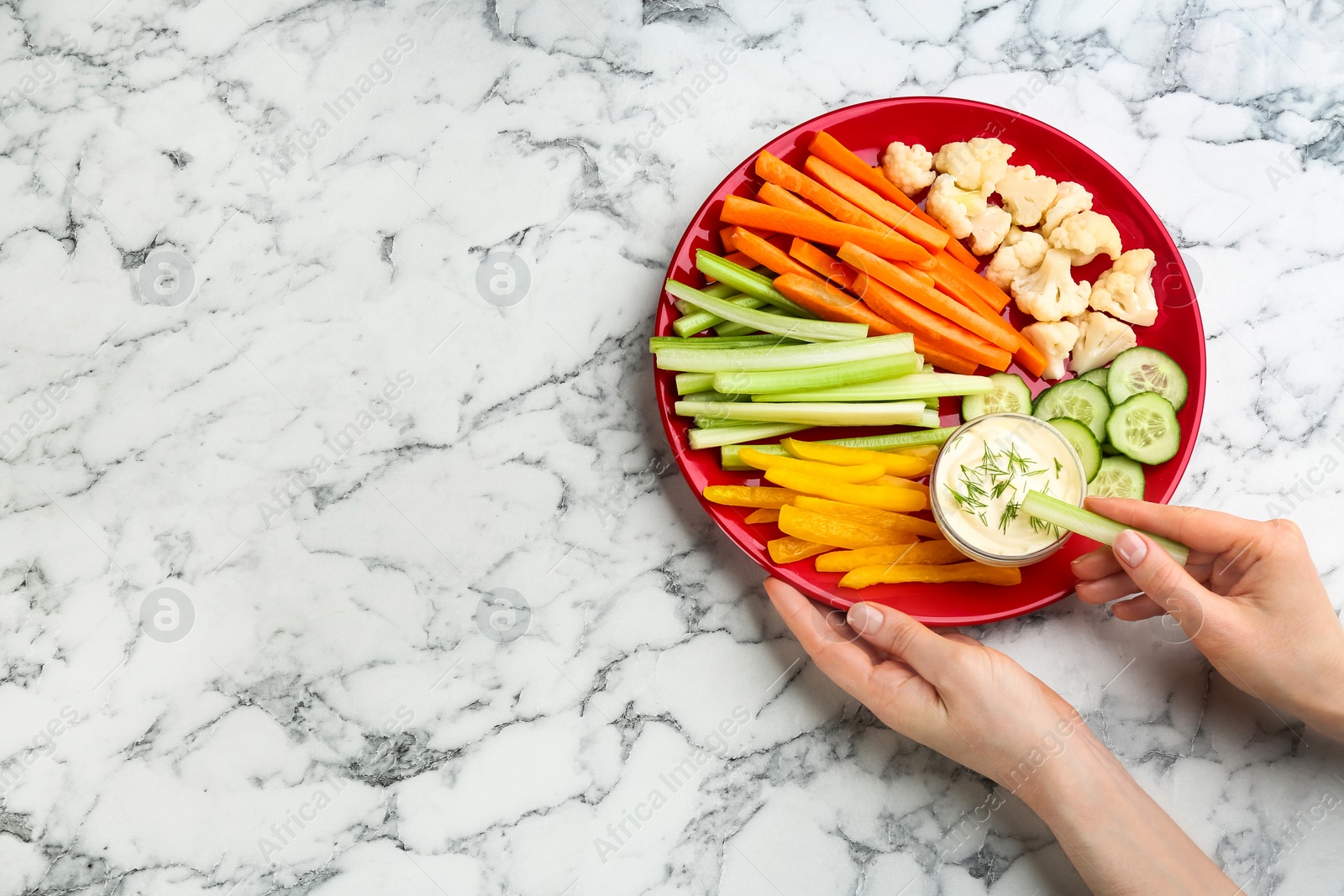 Photo of Woman dipping celery stick in sauce at white marble table, top view. Space for text