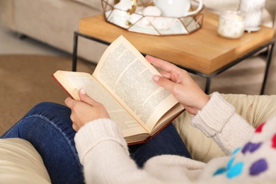 Photo of Woman wearing warm sweater reading book at home, closeup