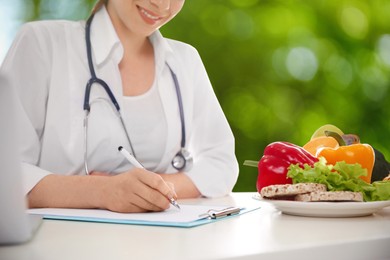 Nutritionist working at table on blurred green background, closeup