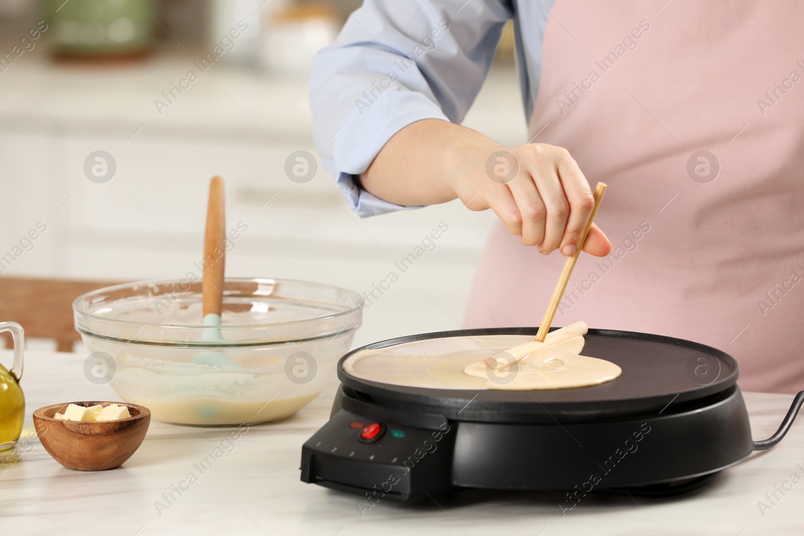 Photo of Woman cooking delicious crepe on electric pancake maker at white marble table in kitchen, closeup