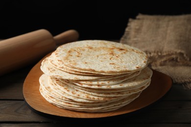 Many tasty homemade tortillas and rolling pin on wooden table