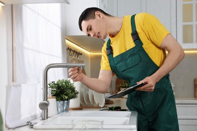 Smiling plumber with clipboard examining faucet in kitchen