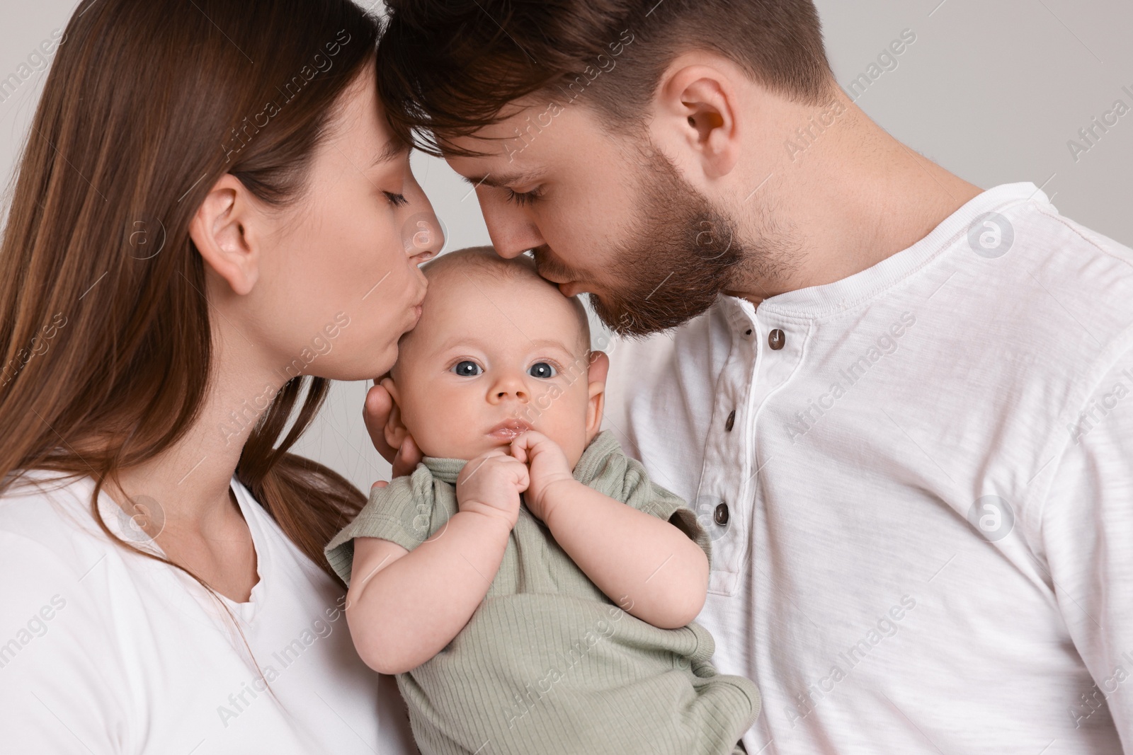 Photo of Happy family. Parents kissing their cute baby on grey background