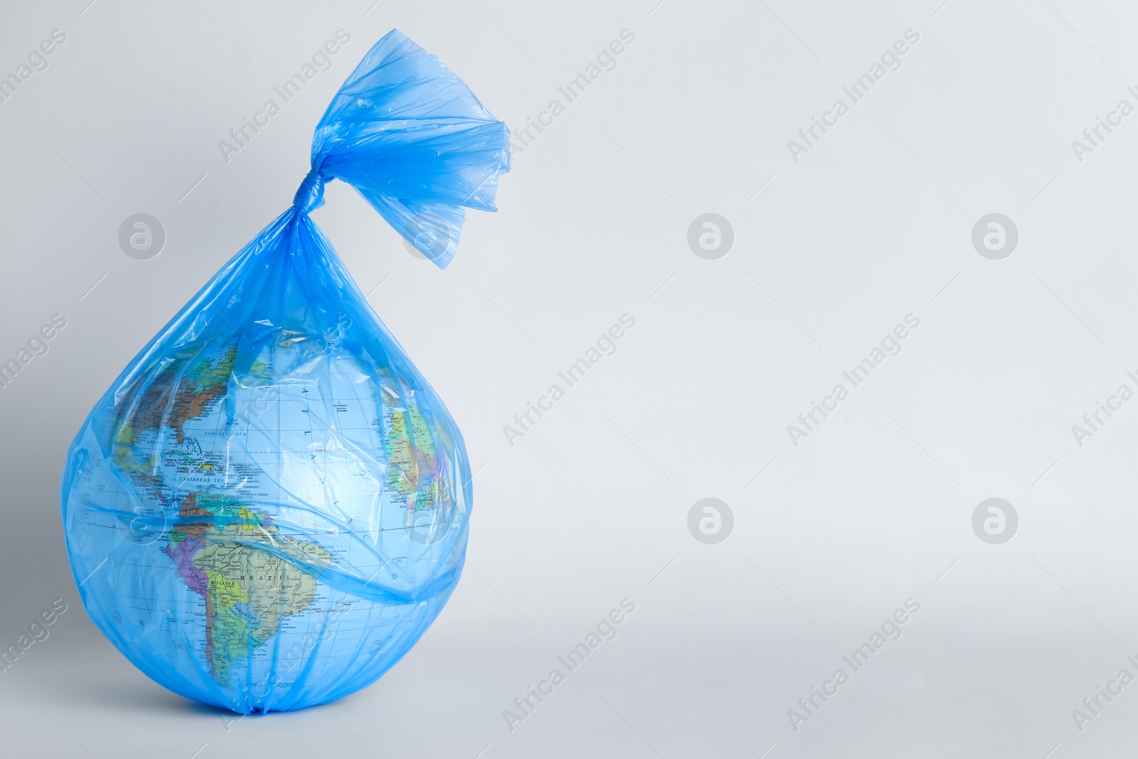 Photo of Globe in plastic bag on light background, space for text. Environmental conservation